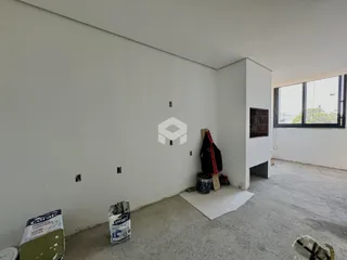 Interior de um cômodo em construção com paredes brancas e piso de concreto.