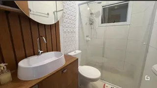 Foto de um banheiro com box de vidro e louças brancas.