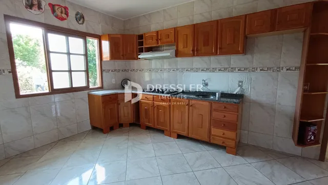 Vista da cozinha e sala de jantar com armários de madeira e piso de cerâmica.