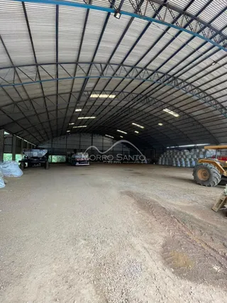 Foto de um espaço amplo coberto com estrutura metálica e piso de terra.