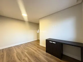 Ambiente interno de uma sala com piso de madeira clara e paredes brancas.