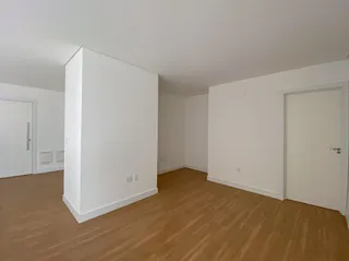 Vista interna de um ambiente com piso de madeira clara e paredes brancas.