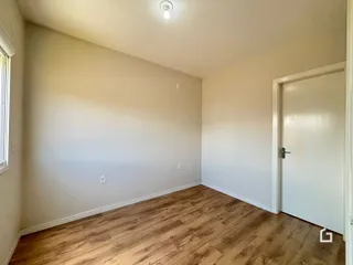 Ambiente interno de uma sala com piso de madeira clara e paredes brancas.