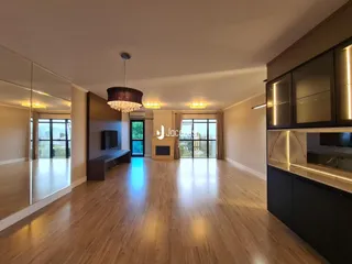 Sala de estar com piso de madeira clara e grandes janelas.