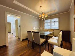 Sala de jantar com mesa de vidro e piso de madeira.