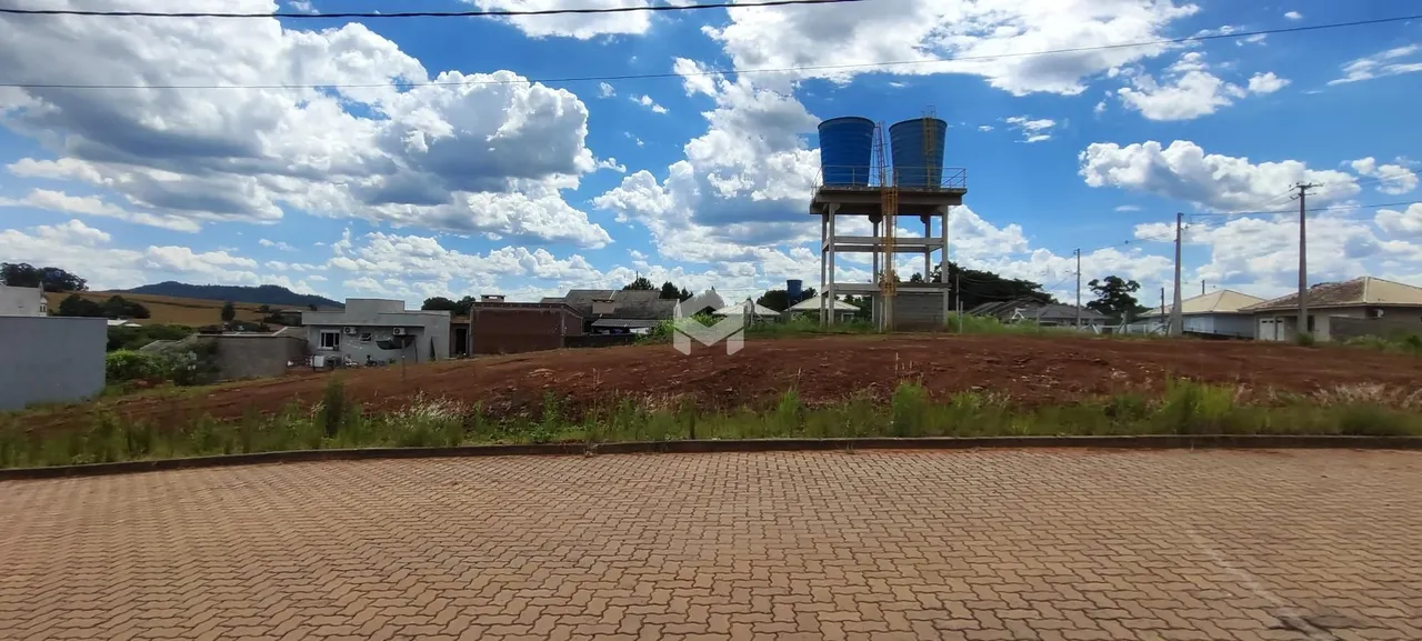 Vista externa de uma propriedade com terreno inclinado e estruturas ao fundo.
