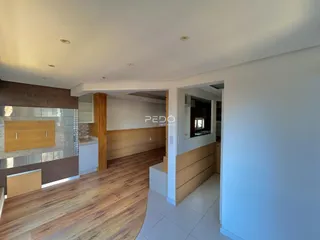Vista interna de uma sala de estar com piso de madeira e paredes claras.