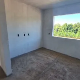 Ambiente interno com paredes brancas e piso de concreto, mostrando uma área vazia.