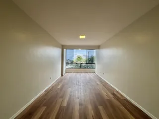 Ambiente interno de uma sala longa com piso de madeira clara.