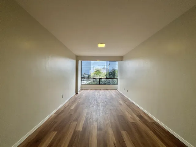 Ambiente interno de uma sala longa com piso de madeira clara.