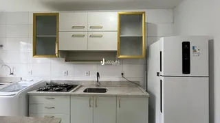 A cozinha exibe armários brancos e bancadas claras com detalhes em dourado.