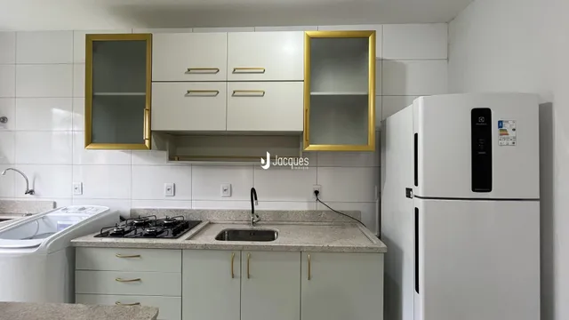 A cozinha exibe armários brancos e bancadas claras com detalhes em dourado.