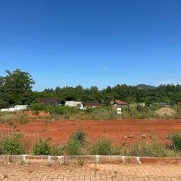 Paisagem de terra vermelha com vegetação no fundo sob um céu azul.