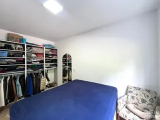 Quarto com cama azul e estante de roupas visível na lateral da sala.