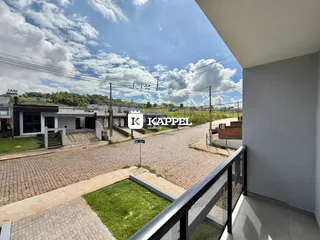 Vista externa mostrando uma área pavimentada e vegetação ao fundo.