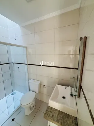 Banheiro com box de vidro e louças brancas.