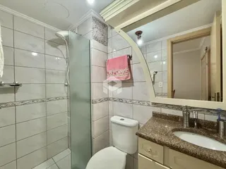 Foto de um banheiro com revestimento cerâmico e box de vidro.