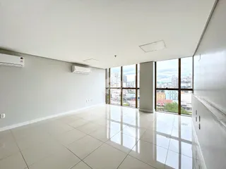 Sala de estar com piso de cerâmica e grandes janelas que oferecem vista da cidade.