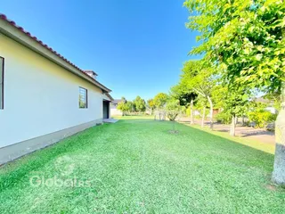 Vista da fachada de uma casa com grande gramado e árvores ao fundo.