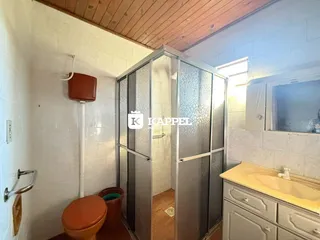 Banheiro com revestimento de azulejos brancos e teto de madeira exposto.