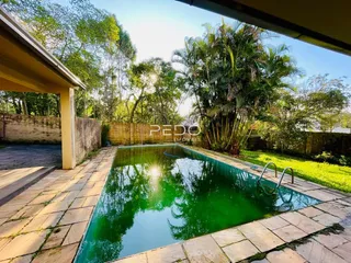 Piscina externa com deck de pedra e vegetação ao fundo.