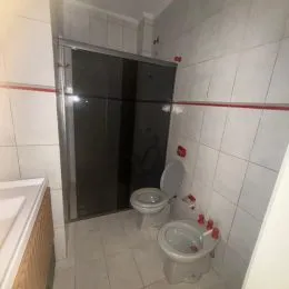 Uma foto interna mostra paredes brancas e revestimento cerâmico de um banheiro.