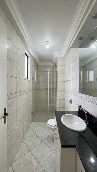 Banheiro com revestimento de azulejos claros e box de vidro transparente.