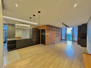 Sala de estar moderna com piso de madeira clara e cozinha integrada.