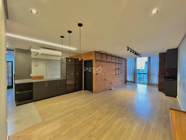 Sala de estar moderna com piso de madeira clara e cozinha integrada.