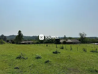 Paisagem de campo verde com estruturas rurais ao fundo.
