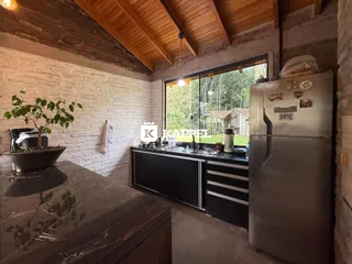 Cozinha com bancada escura e parede de tijolos expostos, com vista para a vegetação externa.