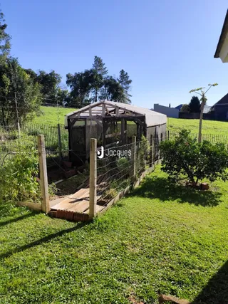 Vista externa de uma propriedade com cerca de madeira e vegetação.