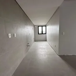 Um corredor interno com paredes claras e uma janela no final.