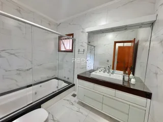 Banheiro com box de vidro e bancada de mármore branco.