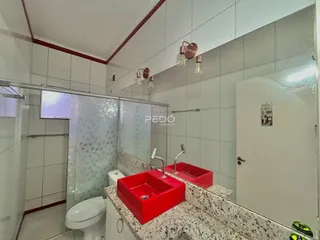 Foto interna de um banheiro com revestimento de cerâmica e pias vermelhas.