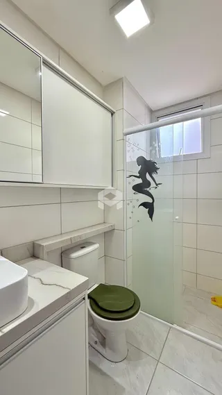 Interior de um banheiro com revestimento branco e box de vidro.