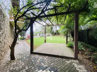 Vista externa de um jardim com parede de pedra e estrutura de madeira.