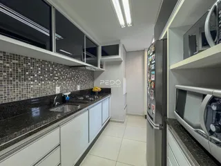 Cozinha moderna com armários brancos e bancadas escuras em um imóvel no Brasil.
