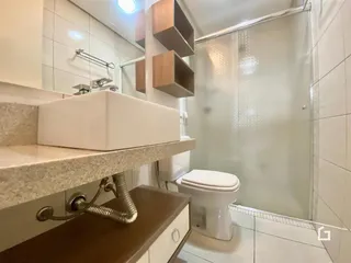 Interior de um banheiro com azulejos brancos e box de vidro.