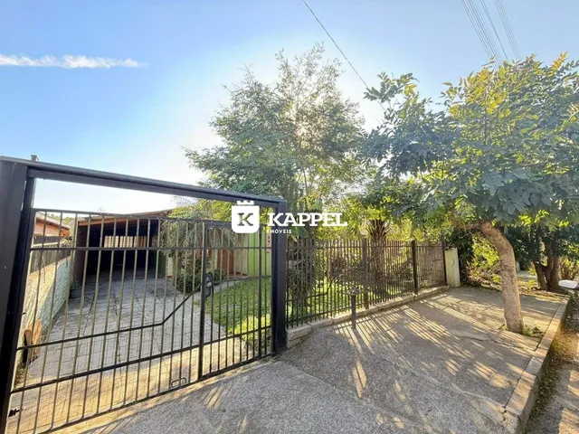 Foto da fachada de uma propriedade com portão de metal e área externa pavimentada.