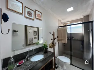 Vista da área de banheiro com bancada de mármore e box de vidro.