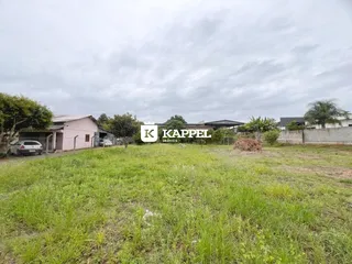 Vista externa de um terreno com grama alta e estruturas ao fundo.