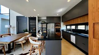 Foto de uma sala de jantar com mesa de madeira e bancada de cozinha escura.