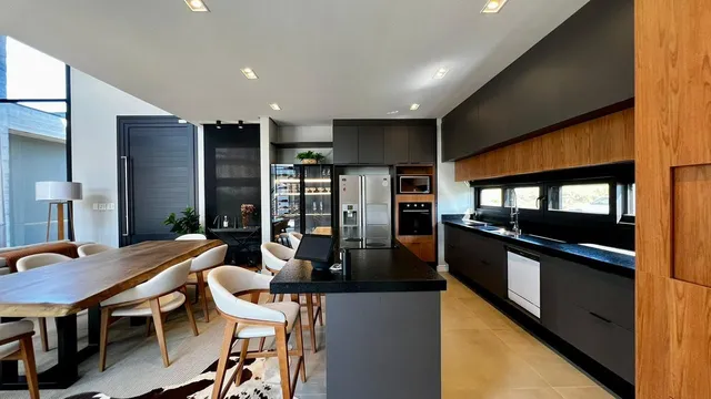 Foto de uma sala de jantar com mesa de madeira e bancada de cozinha escura.