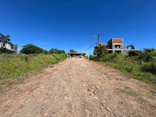 Vista de uma estrada de terra com vegetação rasteira em frente a construções no horizonte.
