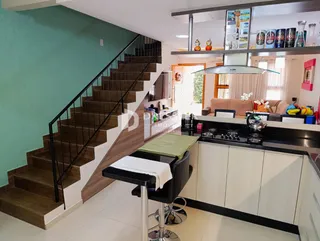 Vista interna de uma sala de estar com escadaria e cozinha em um imóvel no Brasil.