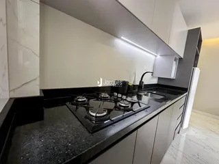 Vista da cozinha com bancada escura e armários brancos.
