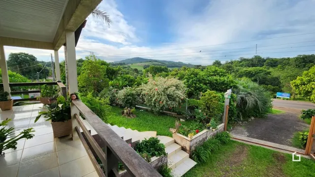 Vista de uma varanda com paisagem verde e colinas ao fundo.