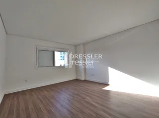 Uma sala com piso de madeira clara e janela iluminada.