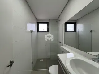 Interior de um banheiro com revestimento cerâmico e box de vidro.